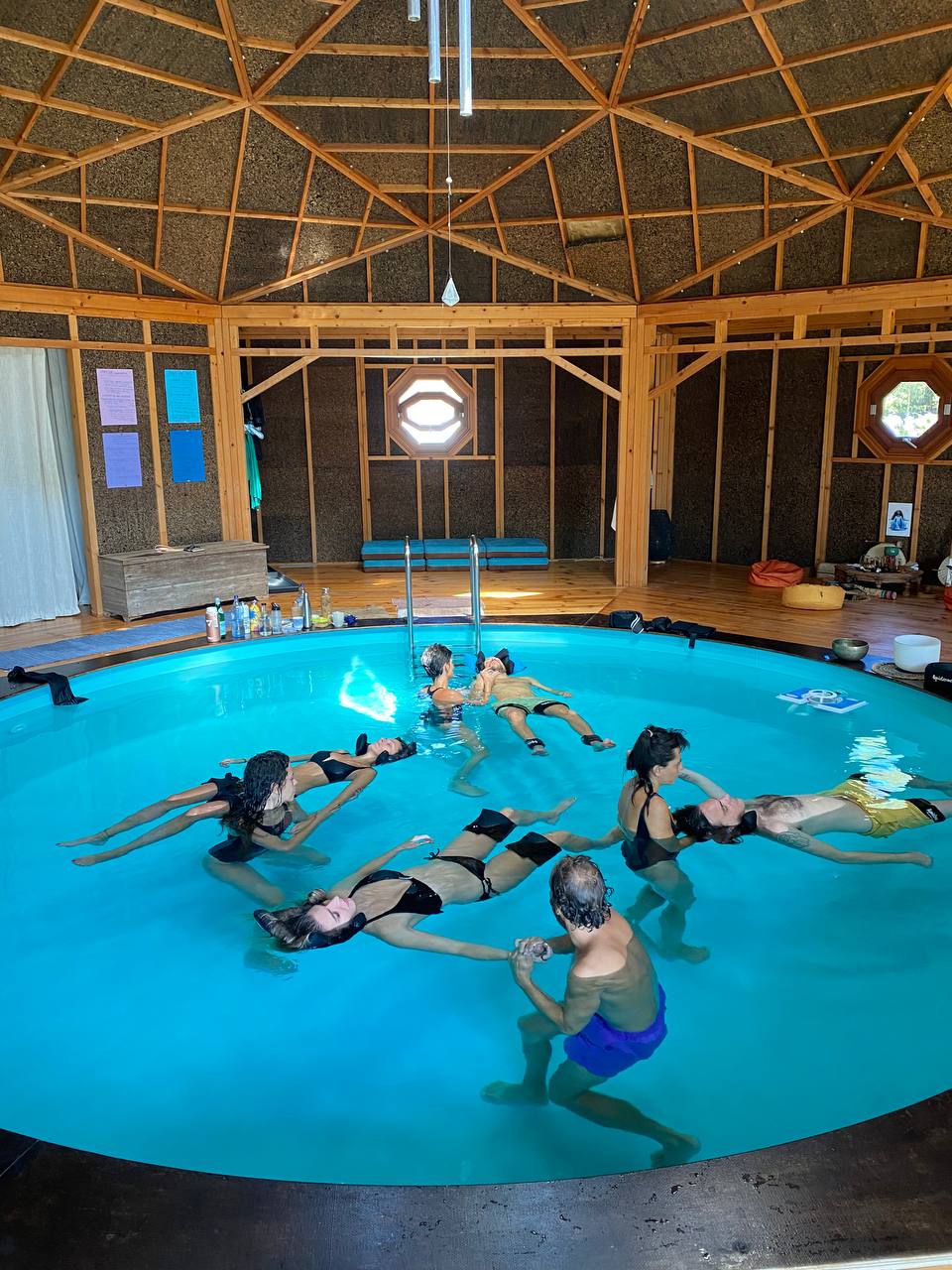 Group floating together in a circular pool inside a wooden geodesic dome
